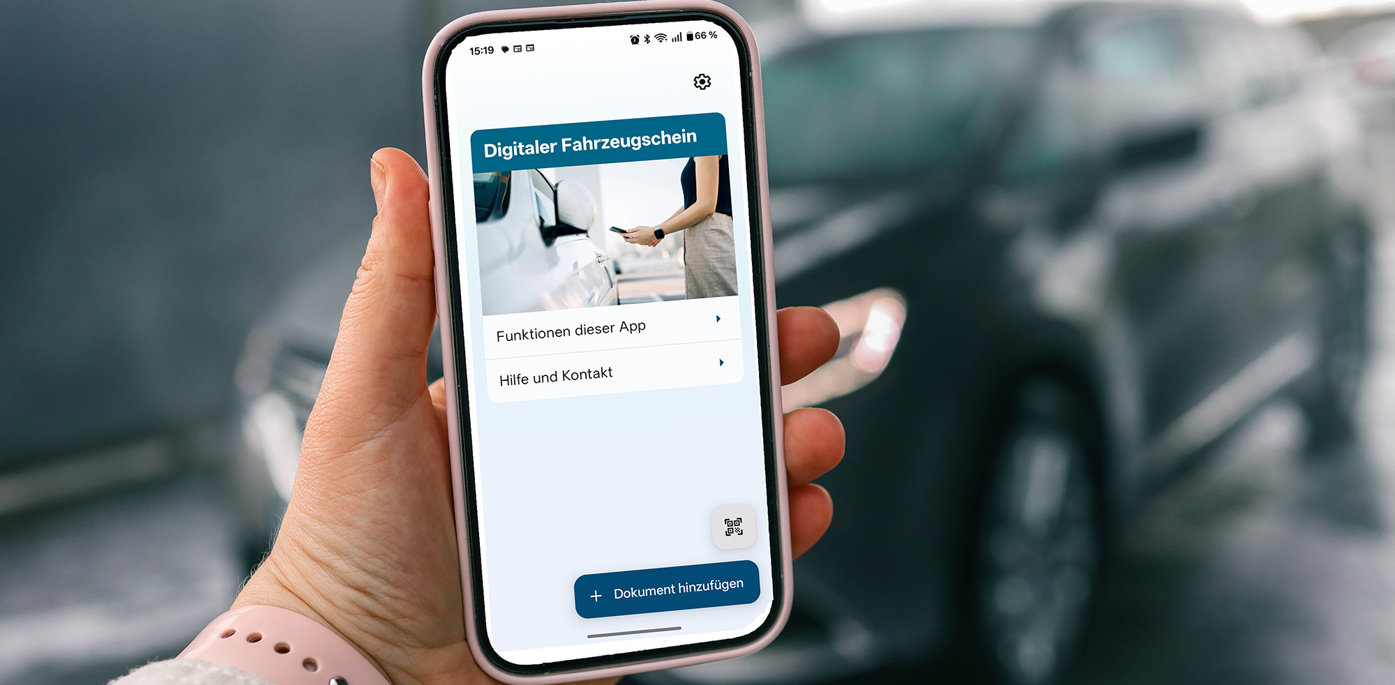 Ansicht der i-Kfz-App auf einem Smartphone vor einem im Hintergrund stehenden Autoshine.graphics/Shutterstock